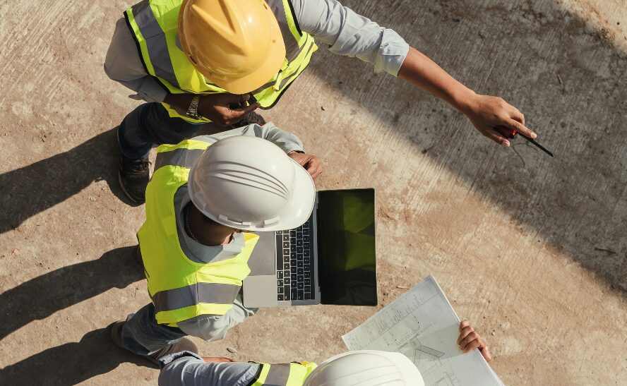 Engineers in hard hats on site reviewing laptop